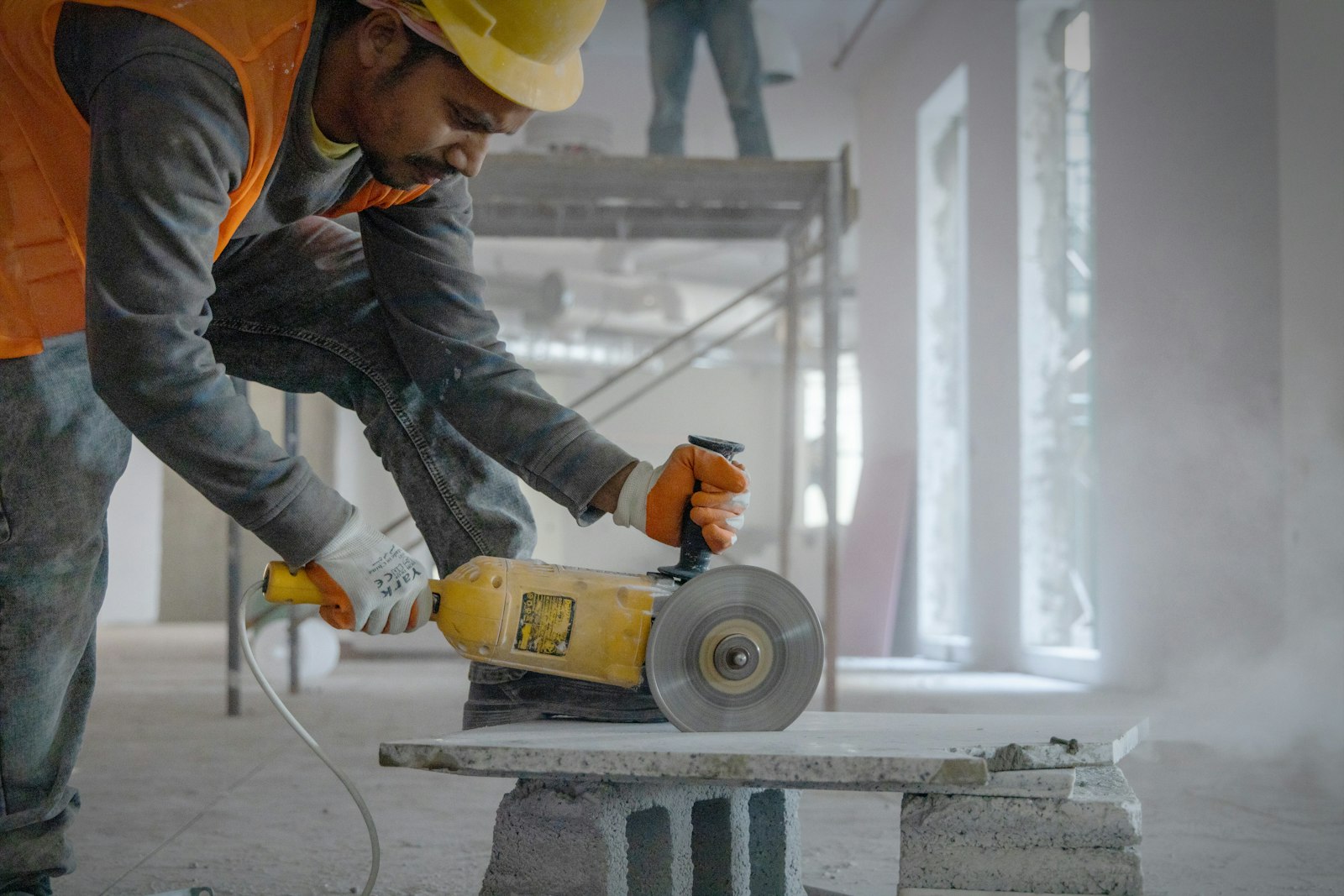 A worker bent over a concrete slab with both hands on a running grinder