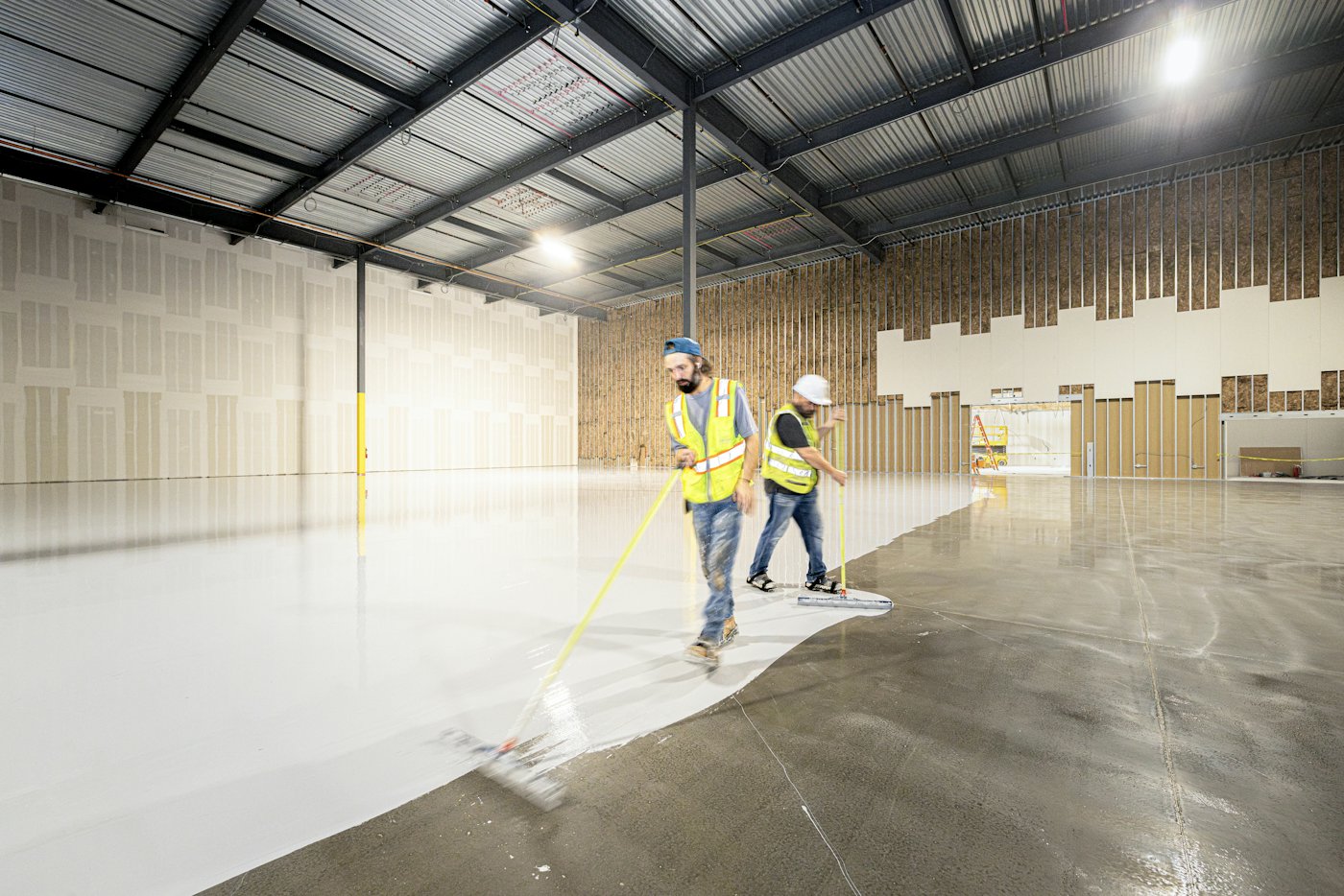Two installers rolling a coating across a warehouse floor