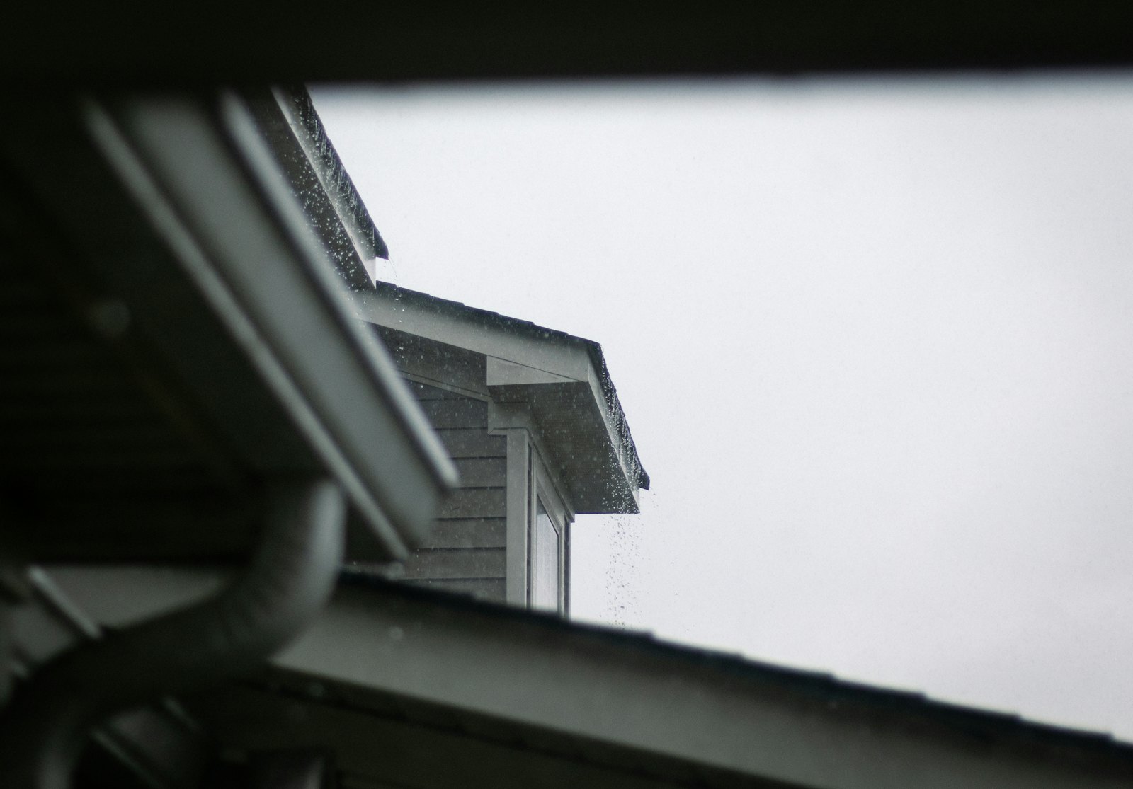 Rain pouring off a roof edge past a downspout